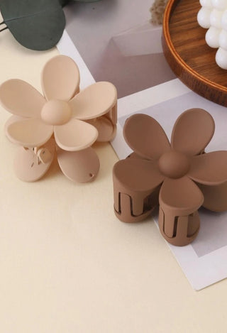 Two flower-shaped hair clips in beige and brown on a light surface.
