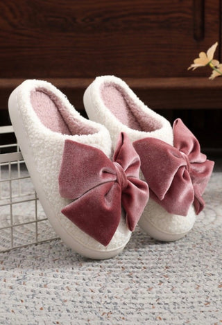 White slippers with pink bows on a carpeted floor.